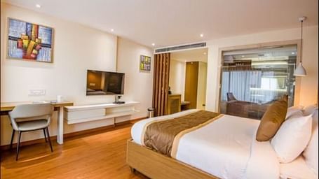 A well-appointed hotel suite with a comfortable bed, a desk area, a large window, and a wall-mounted television, all set within a bright and airy space at Yashshree The Imperial Inn, Siliguri.