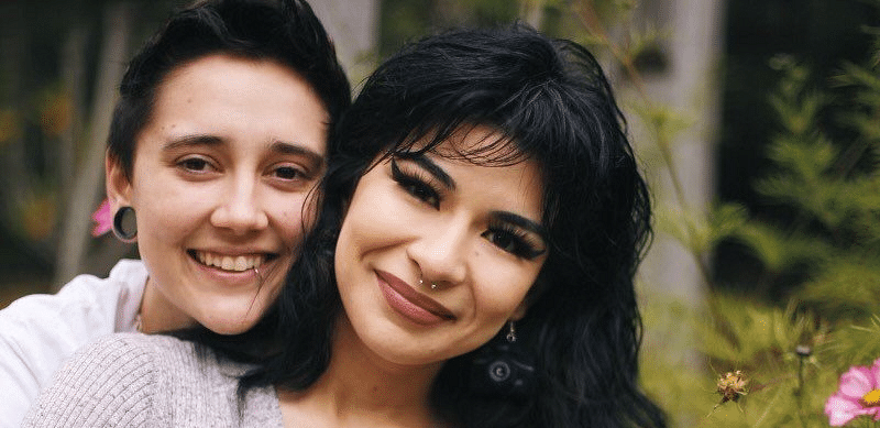 A couple posing for a photo, with the person in the back putting their arms around the person in the front.