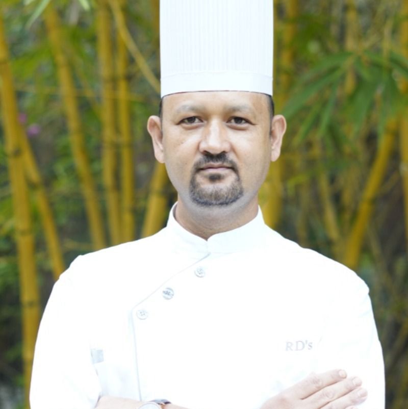 A portrait of a chef at RD’s Nature Retreat, Bangalore, with tall bamboo shoots in the background.
