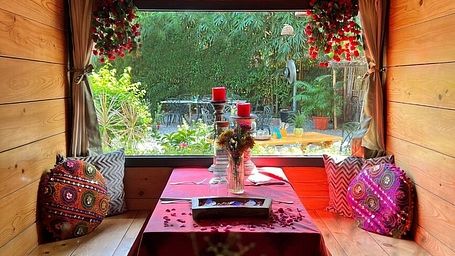 Window-side wooden seating area with red decor and flower vases at Karma Chalets.