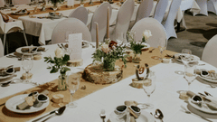 A beautifully decorated rustic-themed wedding reception hall with long tables covered in white tablecloths and hessian runners.
