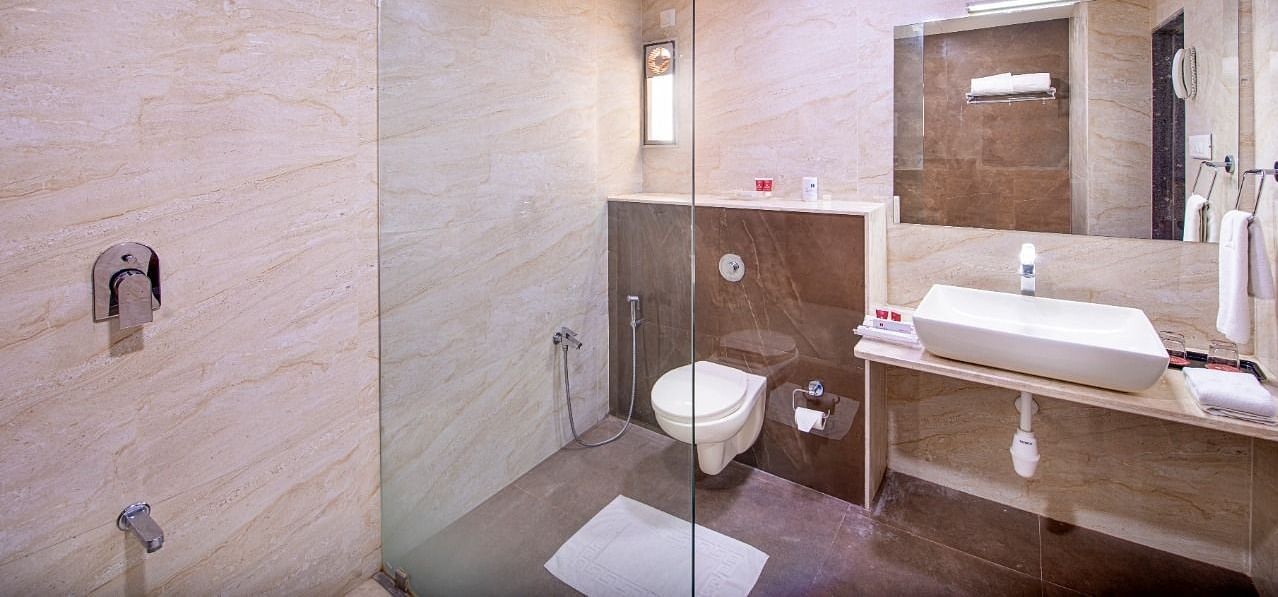 A bright and modern hotel bathroom is equipped with a glass-enclosed walk-in shower, a sleek countertop washbasin, and a toilet.