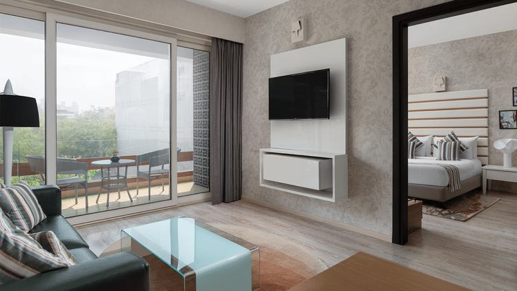 A modern living space at The Atara, Gurugram presented with a wall-mounted TV, a light blue couch with a glass coffee table, and a large sliding glass door that opens to a balcony