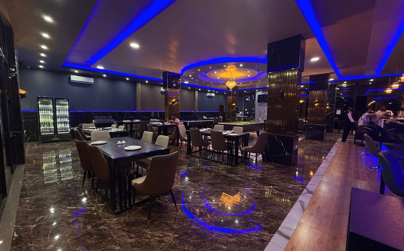 A panoramic view of a restaurant or bar interior, featuring dark decor, shimmering floors, and vibrant blue neon strip lighting at Luffu Club.