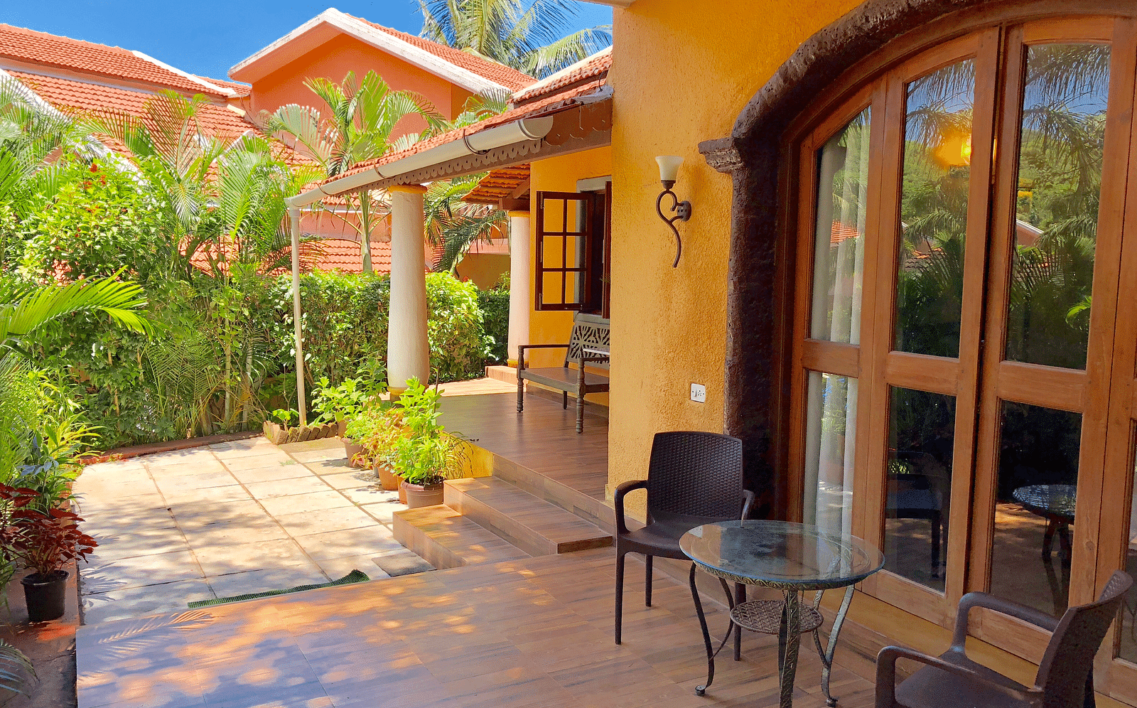 Exterior sitting area during daytime at The Bungalows Light House, Goa featuring a coffee table and a pair of chairs with lush greenery in the surroundings