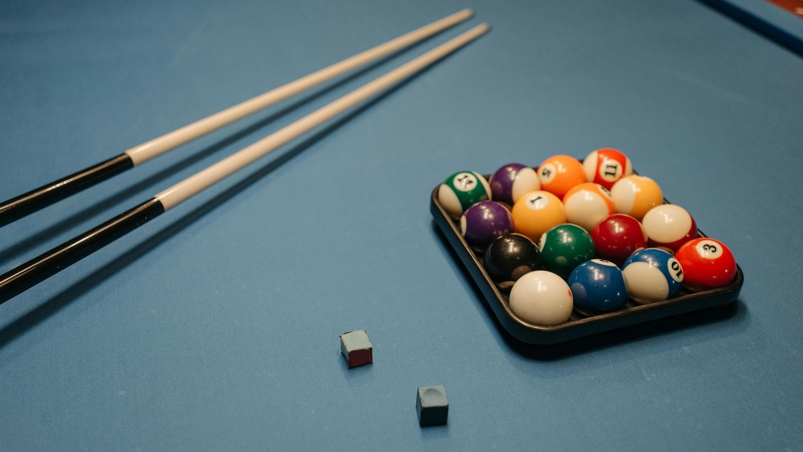 A billiards table with balls, cue sticks, and chalk placed on it.