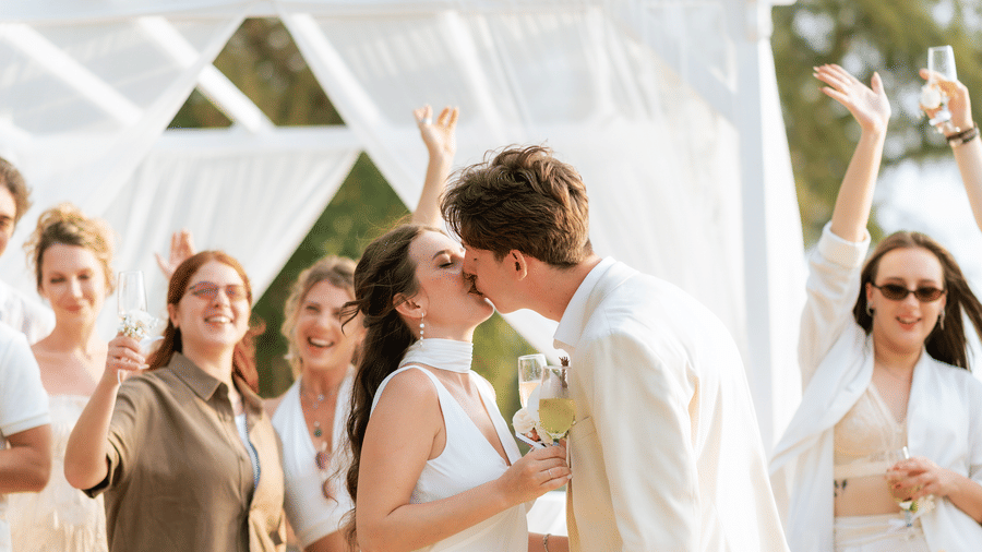 Couple exchanging vows and kiss under a decorated beachside canopy during a wedding ceremony.