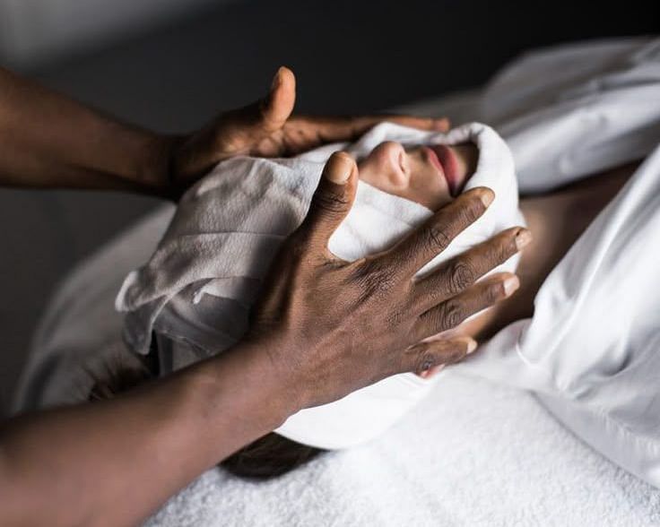Spa therapist gently massaging a client’s face with a warm towel wrap during a facial treatment.