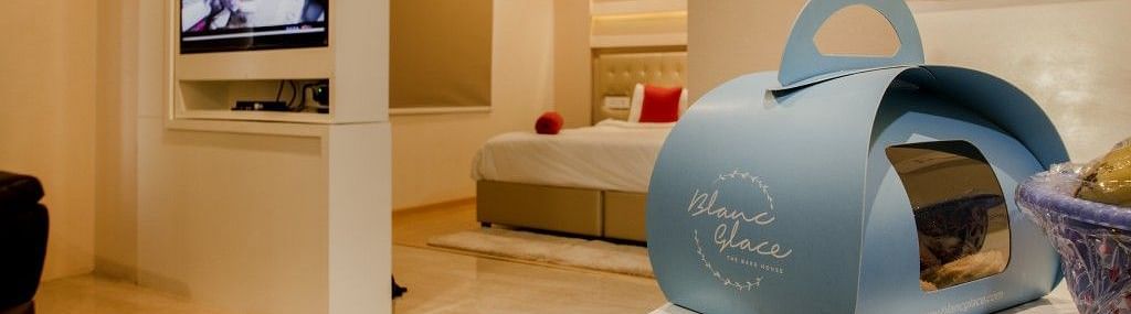 Sitting area of the suite room with a packet of food on the table, a television mounted on the wall and door leading to the bedroom  Art Boutique Hotel, Hyderabad