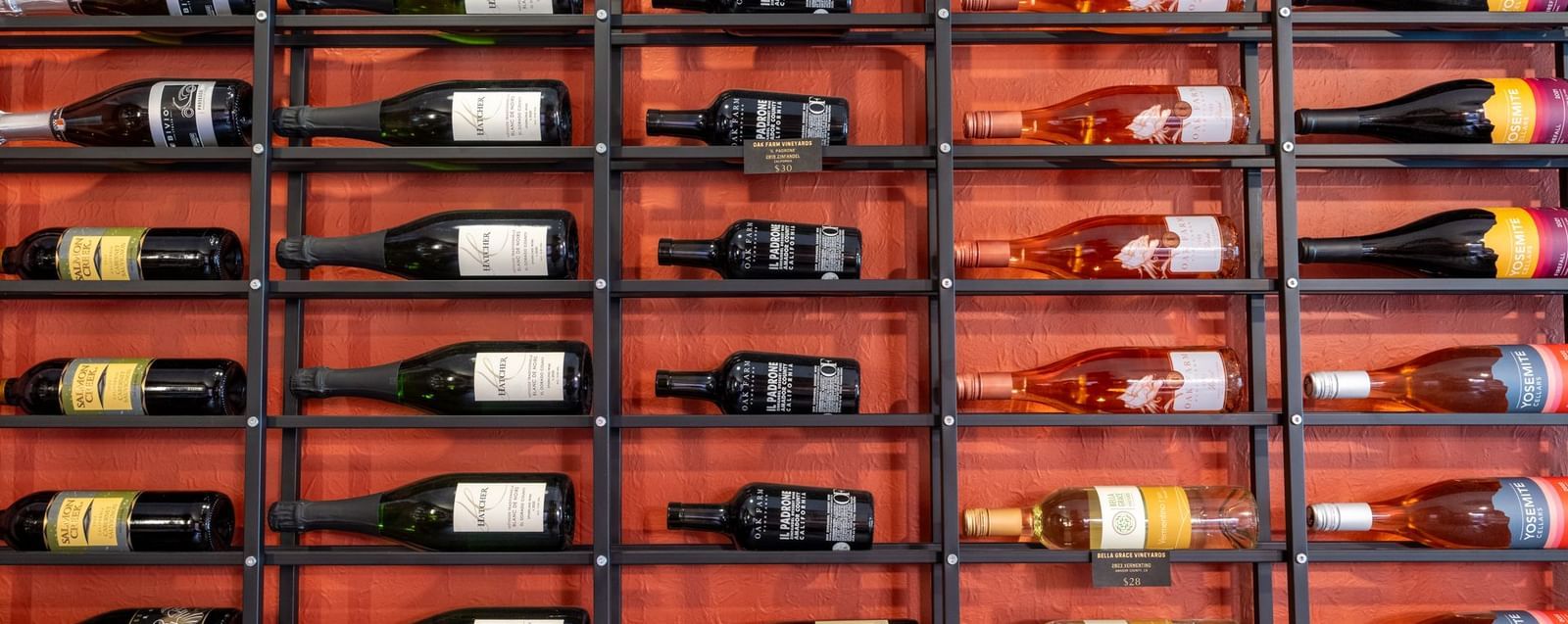  A wide shot of a large metal wine rack, displaying multiple rows of wine bottles on a red wall at Aroma Restaurant and Wine Bar at The Groveland Hotel.