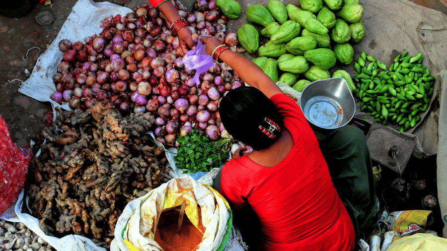 Overhead view of a street vendor selling fresh onions, mangoes, and greens at a bustling local market in Kathmandu, Nepal.