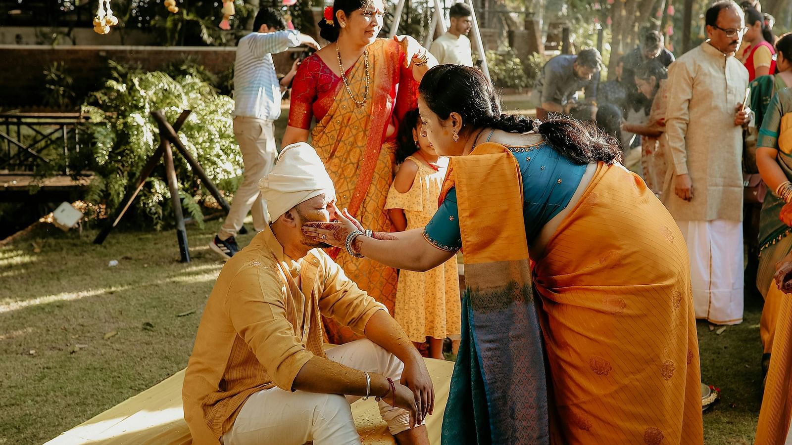 the Indian wedding ritual of haldi being performed in a lawn where a woman is applying turmeric on the groom 