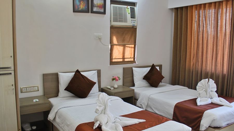 A front view of elegantly decorated twin beds in a room with a window-fitted air-conditioner