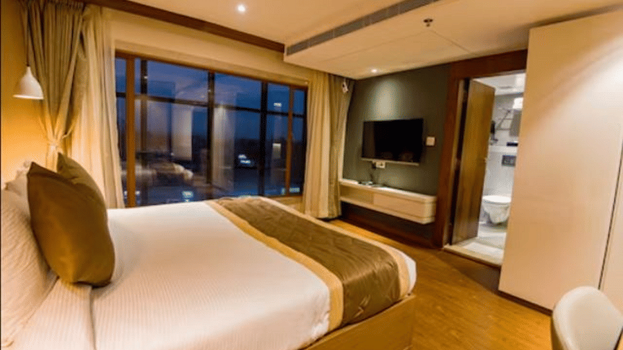 A deluxe hotel room with a large bed, a wall-mounted TV, and windows to the side of the bed at Yashshree The Imperial Inn, Siliguri