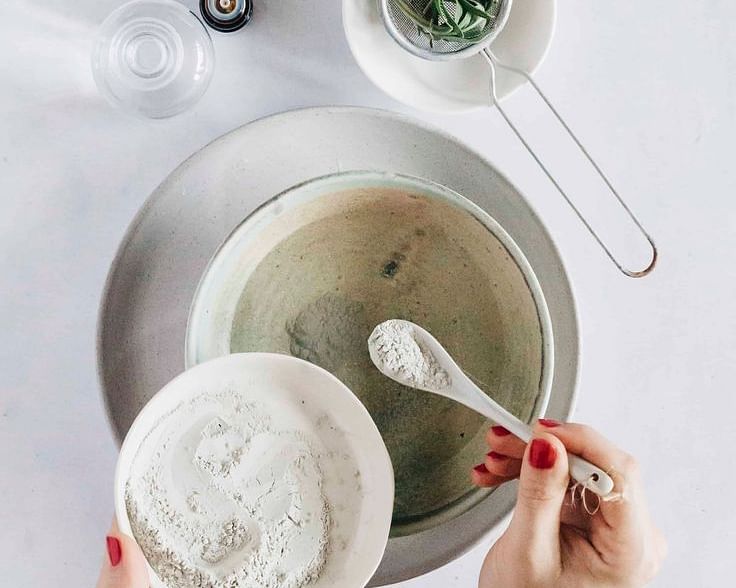 Hands preparing a skincare mixture in a bowl with natural ingredients on a white background.