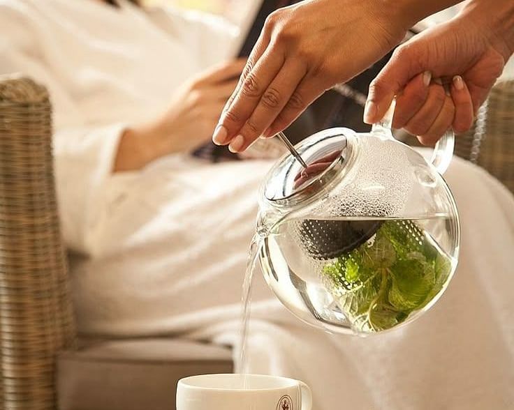 Guest in a spa robe being served herbal tea in a serene and calming spa setting.