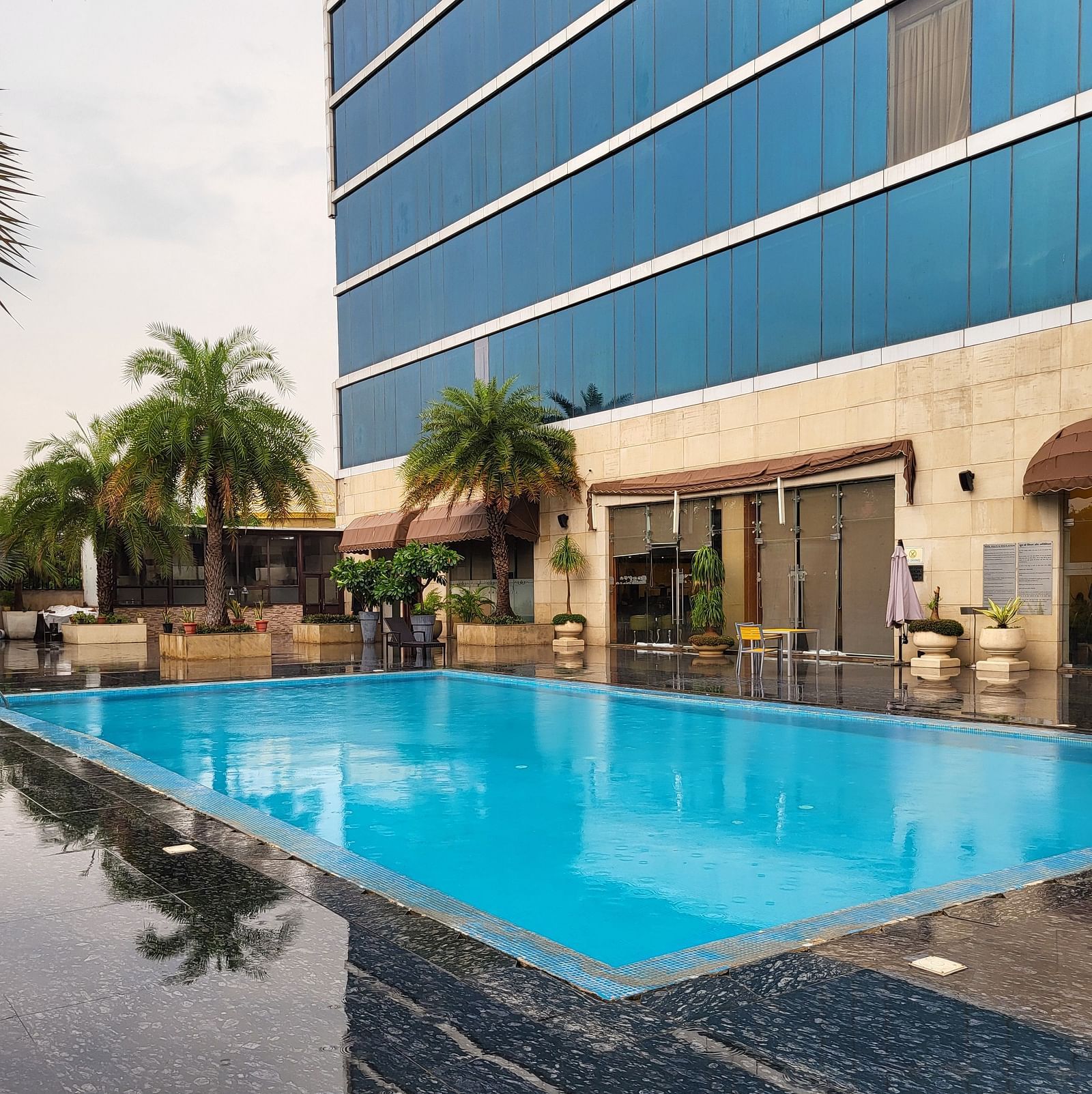 A facade featuring glass walls on the outside and within the property there is a swimming pool and some palm trees Golden Suites Gurgaon