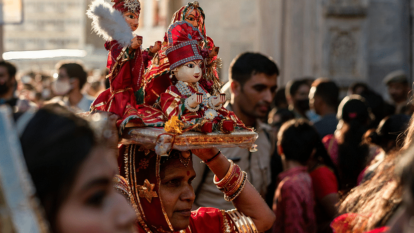 A huge procession celebrating a festival and a woman can be seen holding idols of Gods and Goddess over her head.