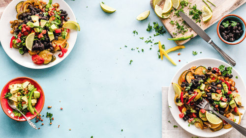 Two sets of dishes placed in front of each other with forks and a knife next to which are limes and cilantro