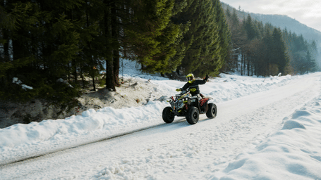 An adventurer riding an all-terrain vehicle (ATV) through a snowy path in a pine forest.