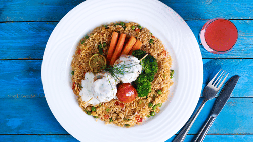 Top-down view of a plated meal with rice, vegetables, sauce, and a drink on a blue wooden table.