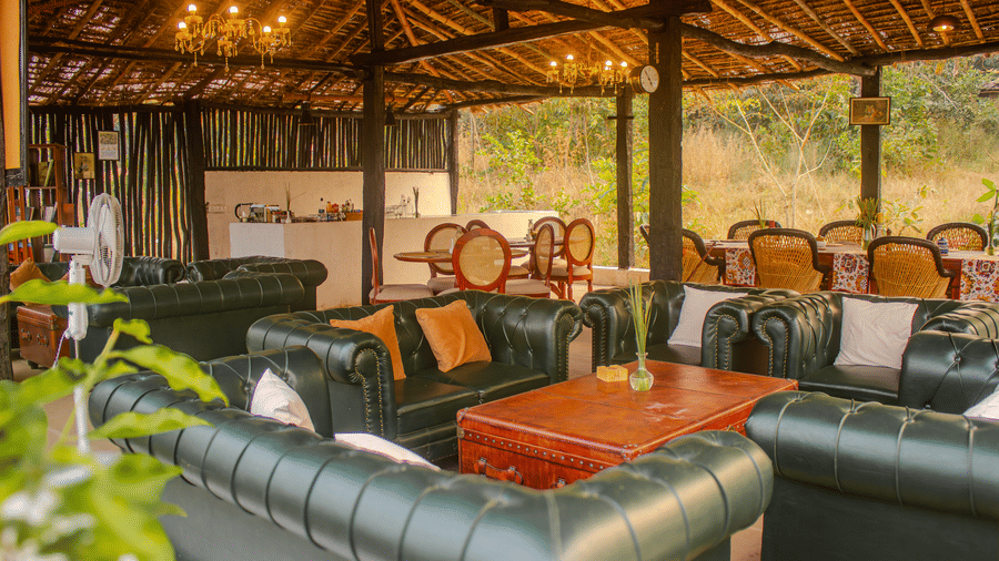 A large open-air lounge and dining pavilion featuring tufted leather sofas under a thatched roof structure - Umaria Safari Camp
