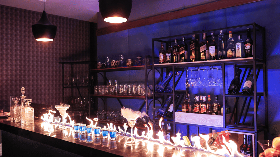 Stylish bar area with bottles on shelving, featuring a long, dramatic flame or dry ice effect across the counter at Hotel Hukam's Lalit Mahal.