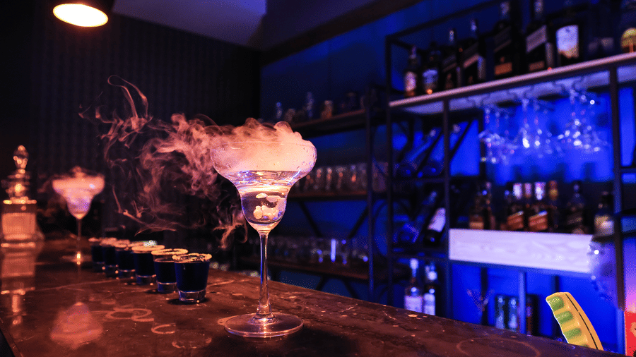 Dramatic bar shot of cocktails lined up with smoky, dry ice effects and strong blue lighting in a dark setting at Hotel Hukam's Lalit Mahal.