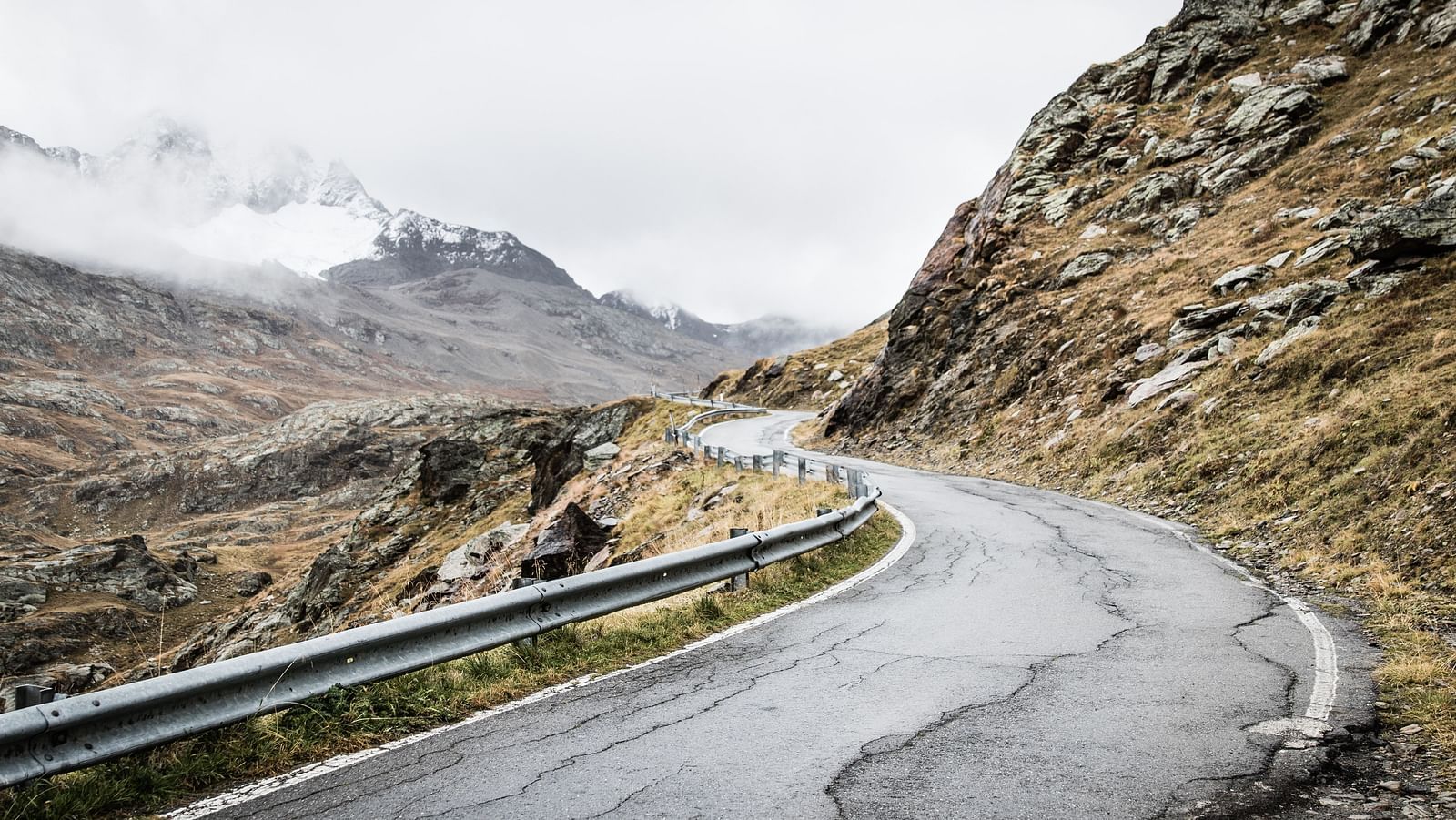 a close up shot of a winding road with a hill on the side and dusky sky in the background.