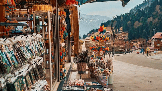 A colourful street market stall displaying vibrant textiles, souvenirs, and trinkets beneath a striped canopy.