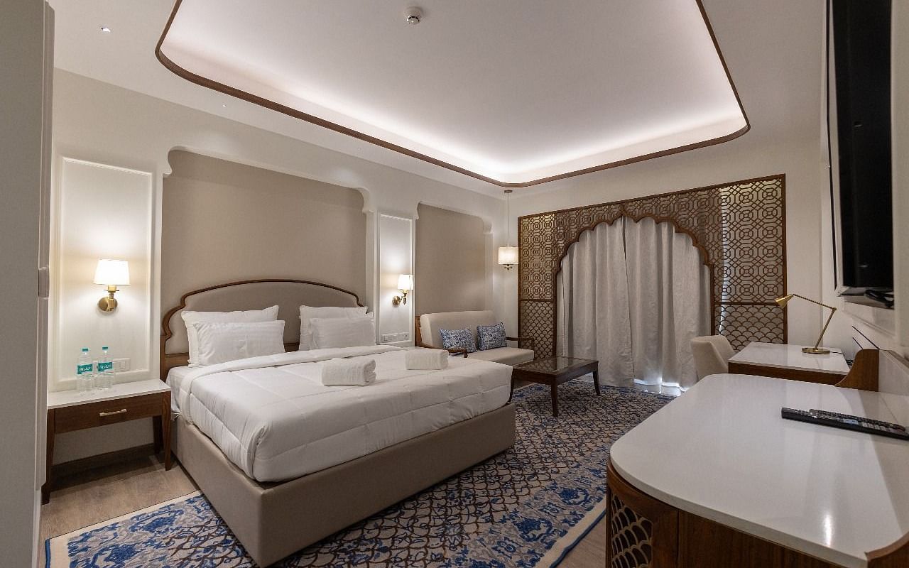 Corner view shot of the Jalrupa Room with a plush double bed placed over a patterned carpet and a common seating area in the corner of the room at Bhagirathi by RDB Atishay.