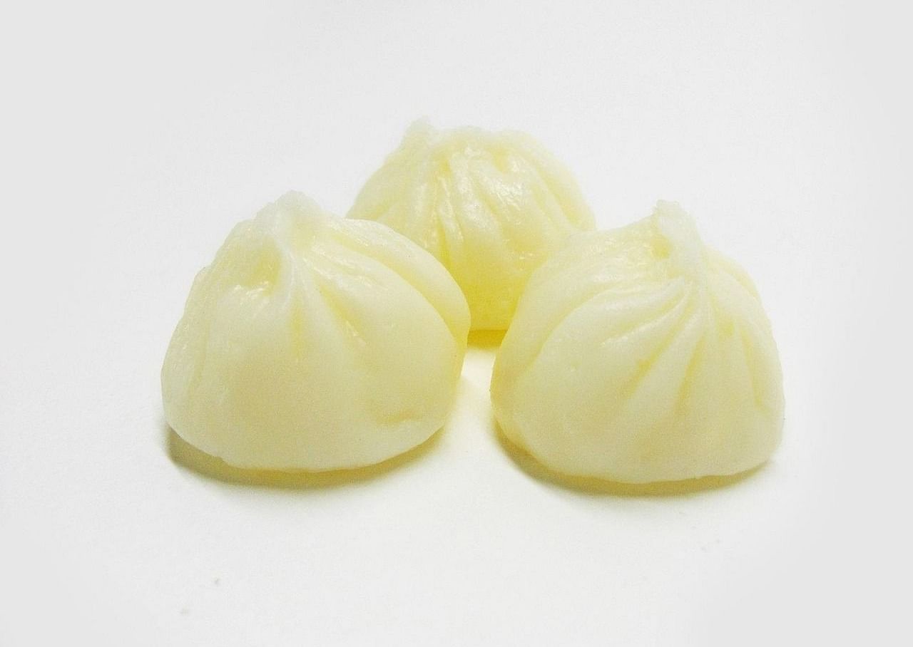 Three white dumplings having intricate handmade carvings kept on a table.