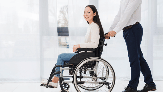 A woman being assisted on a wheelchair by a man.