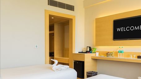 Twin beds with white linens in a room that has a desk and wall-mounted TV | Gemini Continental