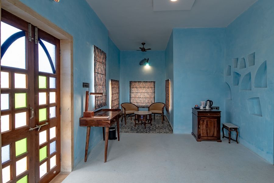 alt-text An image of an indoor seating area with chairs and tables along with a work desk and table at a corner where  tea and coffee maker is kept - Karwaan Jaisalmer