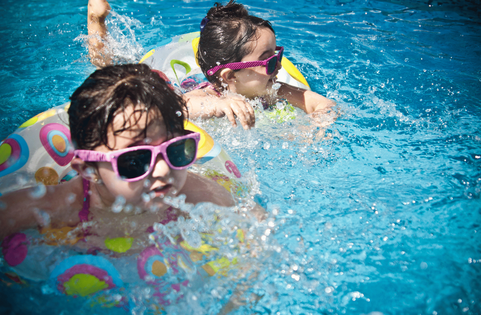 Two children wearing sunglasses enjoying a swim with inflatable rings in a pool.