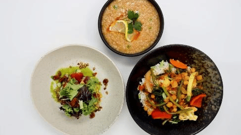 A vibrant trio of healthy dishes plated—fresh salad, hearty soup, and a vegetable stir-fry—served on minimalist black and white crockery at YO1 Longevity & Health Resorts