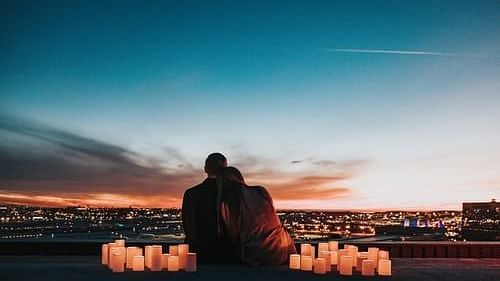a couple embracing each other amidst candles looking at the sun set