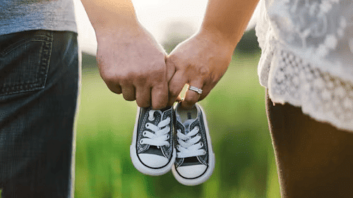 Couple holding baby shoes, symbolising pregnancy announcement or baby shower celebration in a scenic outdoor setting.
