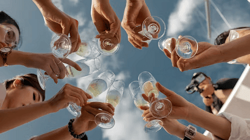 Group of friends raising glasses for a celebratory toast against a bright, sunny sky.