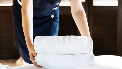 An image of a housekeeping person lifting the clothes for laundry from the bed