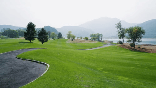 A panoramic shot of the Manesar Golf Course feauturing vast green grassy landscapes with a path for the golf carts.