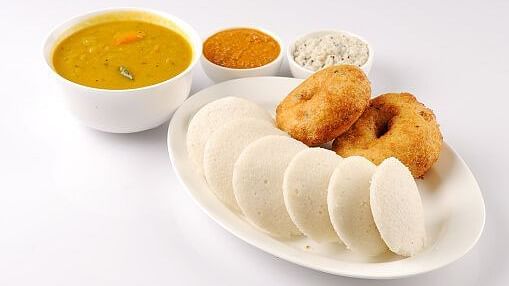 A plate featuring idly and vada, accompanied by three small bowls of side dishes, served at Indie Stays, BKC Kalina.