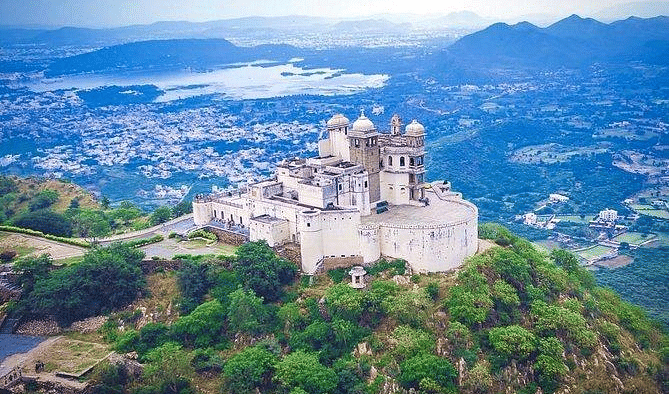 Aerial view of hilltop palace with distant mountains, and city visible.