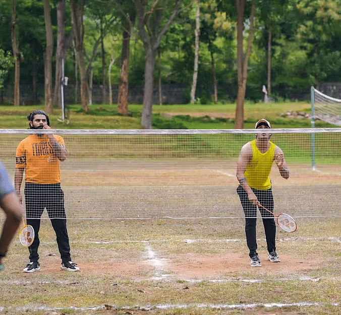 Two men playing badminton, a net with trees behind near Avana Resort