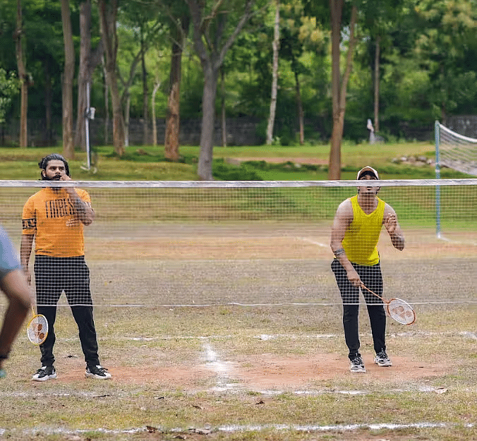 Two men playing badminton, a net with trees behind near Avana Resort