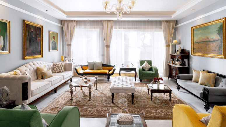 A spacious living room with a mix of modern and classic furniture, including sofas, armchairs, and coffee tables, under a chandelier and with artwork on the walls | Dileep  Kothi, Jaipur