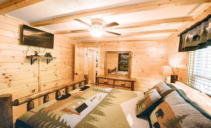 a bedroom featuring a plush double bed with a wall mounted television right opposite to it with a window behind the bed - Historic Tapoco Lodge