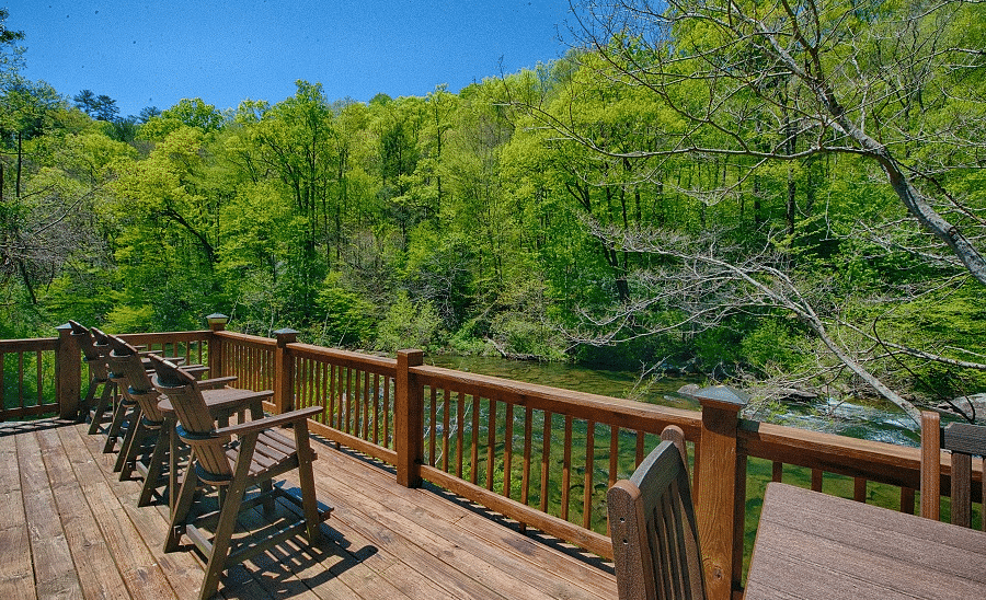 a wooden porch protected by hand railings with several wooden chairs lined up facing towards the forest - Historic Tapoco Lodge