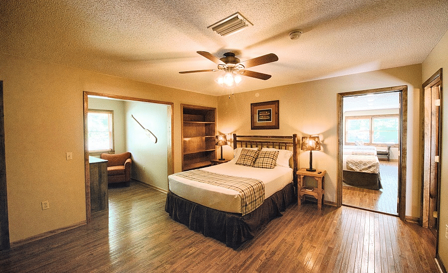 a room with wooden flooring featuring a cozy double bed with a ceiling fan right above it - Historic Tapoco Lodge